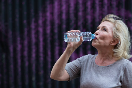 Elderly woman drinking bottled water after training