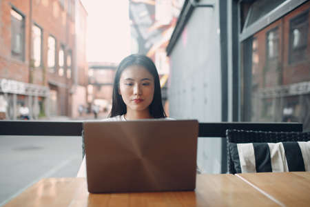 Portrait of asian japanese or korean woman student enjoying using laptop sitting at outdoor cafe.の写真素材