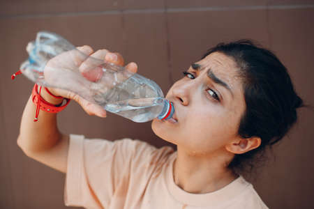 Indian woman drinking bottled still water outdoor wall. Sweat drops on face and heatstrokeの素材 [FY310172018586]