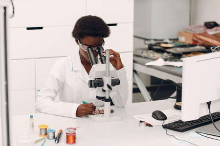 Scientist african american woman working in laboratory with electronic tech instruments and microscope. Research and development of electronic devices by color black woman.の写真素材
