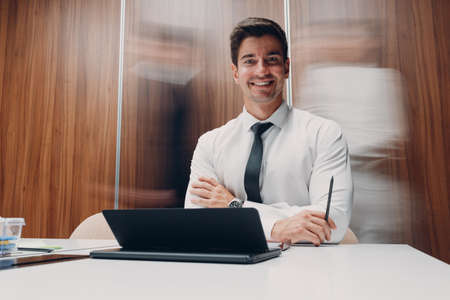 Businessman using laptop sit at table in office meeting background with walking people with motion blur. Business people man and woman group conference discussion.の写真素材