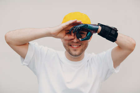 Young disabled man looking binoculars gesture with artificial prosthetic hand in casual clothesの写真素材