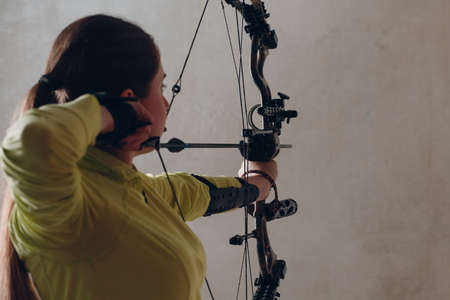Archer woman with modern block sport bow and arrow indoor.