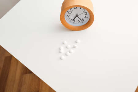 Alarm clock and white blue pills on white table background.の写真素材