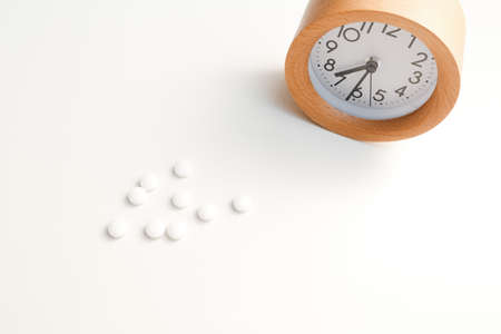 Alarm clock and white blue pills on white table background.の写真素材