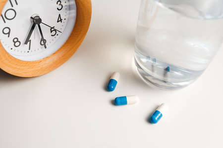 Alarm clock and white blue pills on white table background.の写真素材