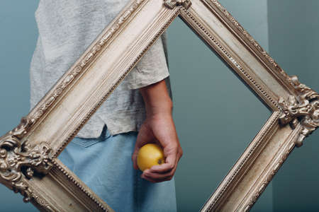 Millenial young man holds apple on hand palm in gilded picture frameの写真素材