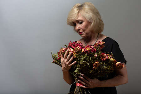 Upset elderly woman hold withered dry old rose flowers bouquetの写真素材