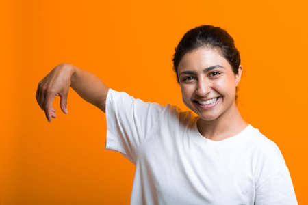 Portrait of young smiling adult indian woman with empty hand holding something with fingers. Advertising template with copy space.の写真素材