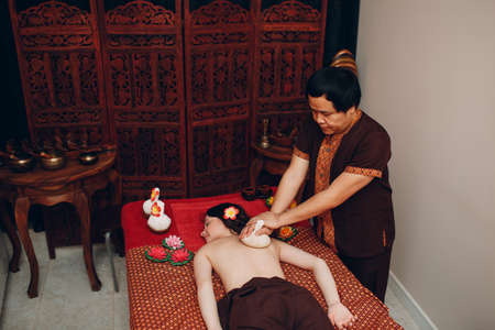 Thai man making classical thai massage procedure to young woman at beauty spa salonの写真素材