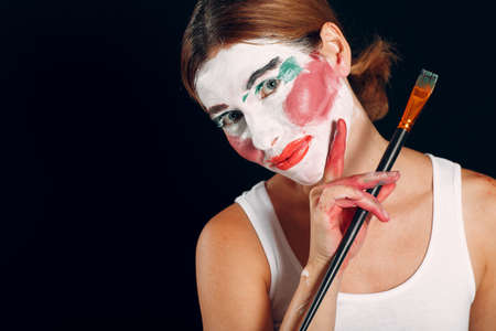 Young woman applying make-up, paints face with painting brush and makeup. How not to do make up concept circus clownの写真素材