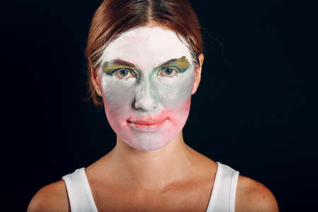 Young woman applying make-up, paints face with painting brush and makeup. How not to do make up concept circus clownの写真素材