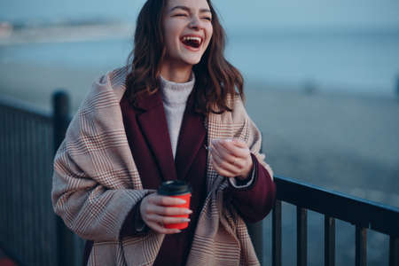 Young beautiful woman in coat and scarf with coffee cup outdoorの写真素材