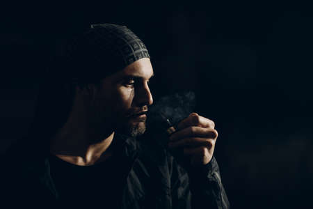 Man smokes smoking pipe against dark background. Back side lit profile portrait with smokeの写真素材