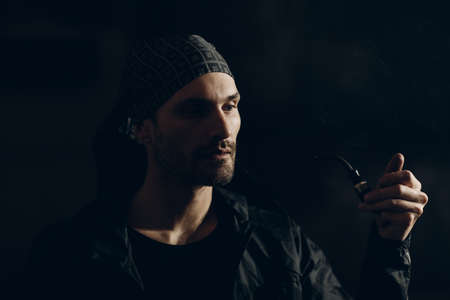 Man smokes smoking pipe against dark background. Back side lit profile portrait with smokeの写真素材