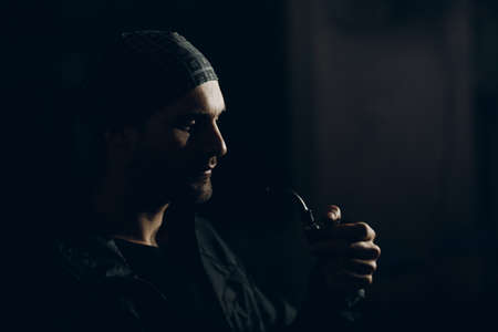 Man smokes smoking pipe against dark background. Back side lit profile portrait with smokeの写真素材