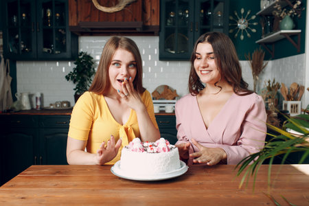 Women happy friends at home sitting and smiling with white birthday cake.の写真素材