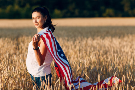 Woman with American flag in wheat field at sunset. 4th of July. Independence Day patriotic holidayの写真素材
