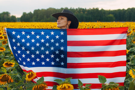 Young woman with American flag in the sunflower field. 4th of July Independence Day USA concept