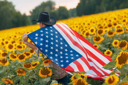 A man is walking into the sunflower field with United States flag. 4th July Independence Day conceptの写真素材