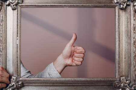 Thumbs up on gilded picture frame pink background