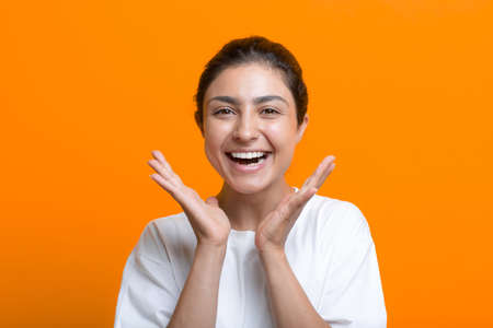 Portrait of positive smiling young adult indian woman in t-shirt hands near face