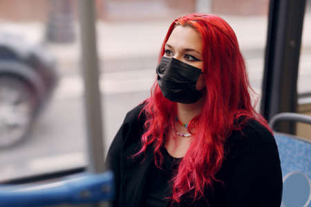European plus size woman face mask riding bus transport. Young red pink haired body positive girl with facemaskの写真素材