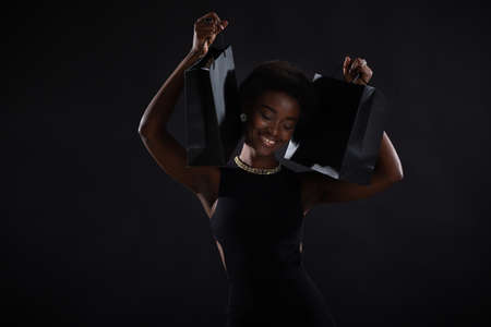 African american happy woman with afro hairstyle holds black shopping bags. Black Friday concept.の写真素材