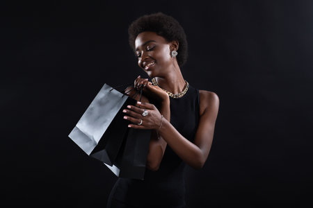 African american woman with afro hairstyle holds black shopping bags. Sale and discounts on retail market and Black Friday concept.の写真素材