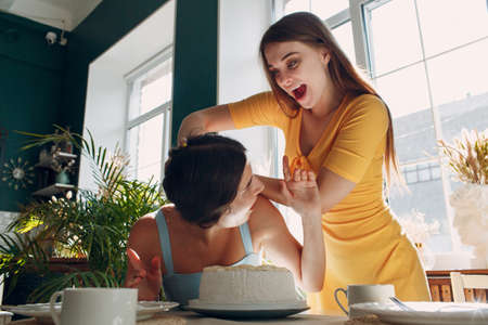 Young woman dips face in white cake with cream. Happy birthday conceptの写真素材