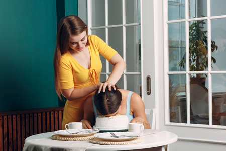 Young woman dips face in white cake with cream. Happy birthday conceptの写真素材