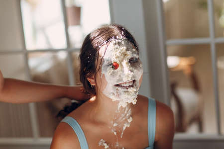 Young woman dips face in white cake with cream. Happy birthday concept