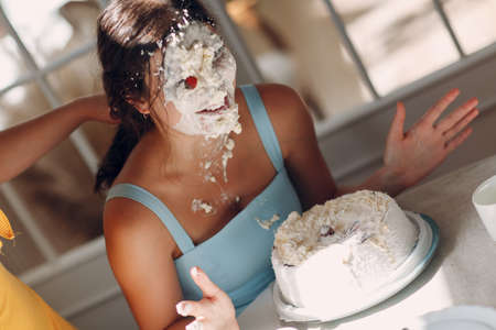 Young woman dips face in white cake with cream. Happy birthday conceptの写真素材