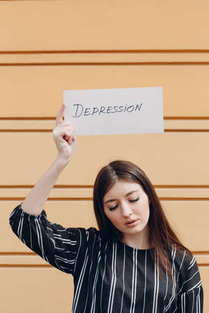 Woman holding white sheet paper labeled word Depression in hand yellow backgroundの写真素材