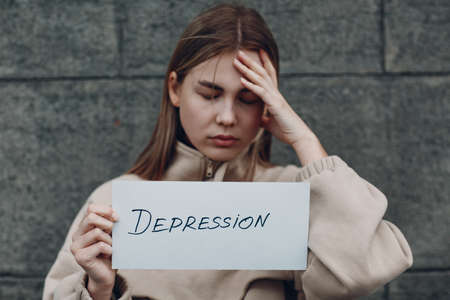 Girl holds in hand sheet of paper with word Depression. Woman with headache touching head.の写真素材