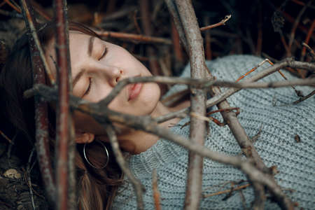 Teenager young woman lying outdoor in the park under dry tree branches. Sex maniac crime rape violence conceptの写真素材