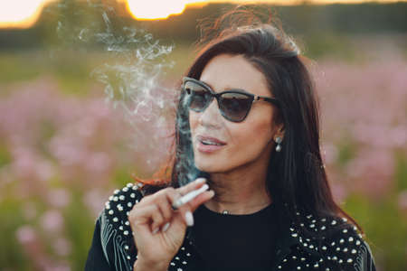 Young woman smoking on blooming Sally flower field. Lilac flowers and womanの写真素材