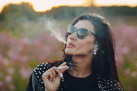 Young woman smoking on blooming Sally flower field. Lilac flowers and womanの写真素材