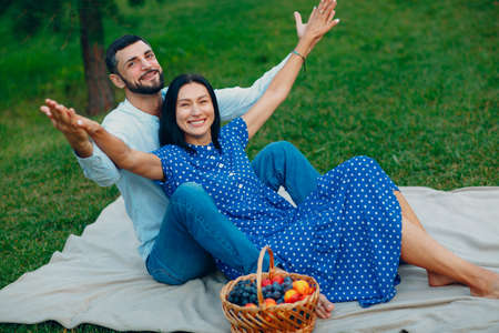 Young adult woman and man couple picnic at green grass meadow in park with open arms.の写真素材