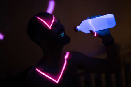 Young adult man drinking bottled water in ultraviolet light.の写真素材