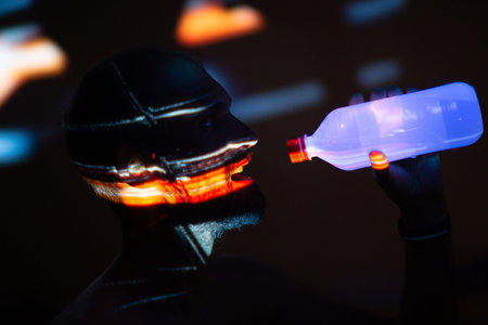 Young adult man drinking bottled water in ultraviolet light.の写真素材