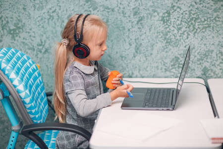 Young student little girl with carrot in hand and laptop learning and preparing back to school.の写真素材