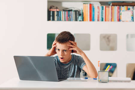 Young boy in headset sitting at table with laptop and preparing to school. Online education conceptの写真素材