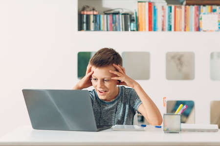 Young boy in headset sitting at table with laptop and preparing to school. Online education conceptの写真素材