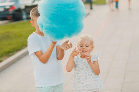 Happy children boy and girl eating blue cotton candy outdoors.の写真素材