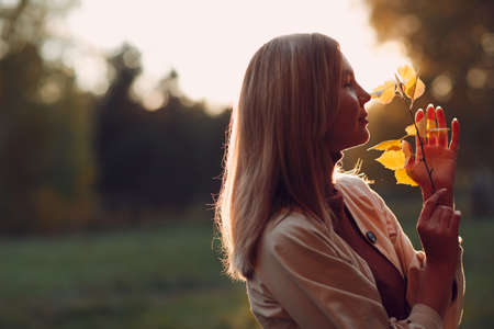 Happy young woman holds fall leaves in hand at autumn park.の写真素材