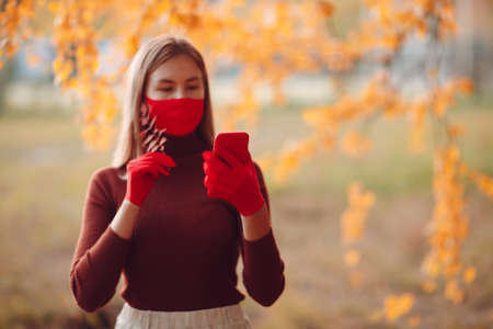 Active young woman in red gloves and face mask at autumn park with mobile phone.の写真素材