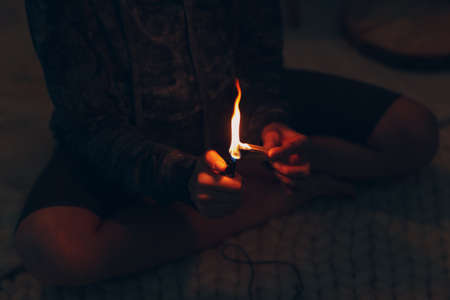 Adult mature woman doing yoga at home living room sets fire with palo santo stick treeの写真素材