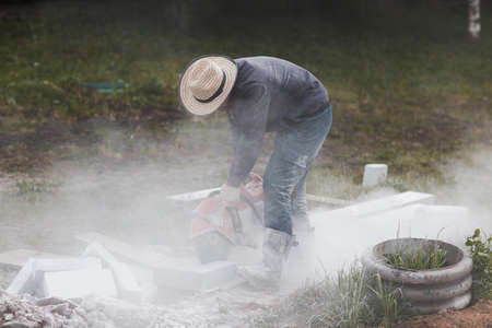 Worker mason cuts the sidewalk tile with circular saw while repairing sidewalk in city street.