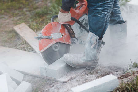 Worker mason cuts the sidewalk tile with circular saw while repairing sidewalk in city street.の写真素材